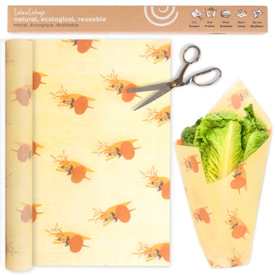 Wax wrap with carrot pattern, scissors, and wrapped leafy greens on a white background