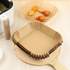 Beige parchment air fryer liners sitting on a wooden cutting board on a light surface, next to an air fryer.