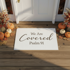 White doormat with "We Are Covered Psalm 91" printed on it, in front of white door with autumn decor on each side