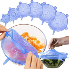 Blue silicone lids being used to cover bowls of fruit and vegetables on a white background