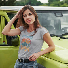 Woman wearing an 'Adventure Seeker' t-shirt leaning against a green vehicle.